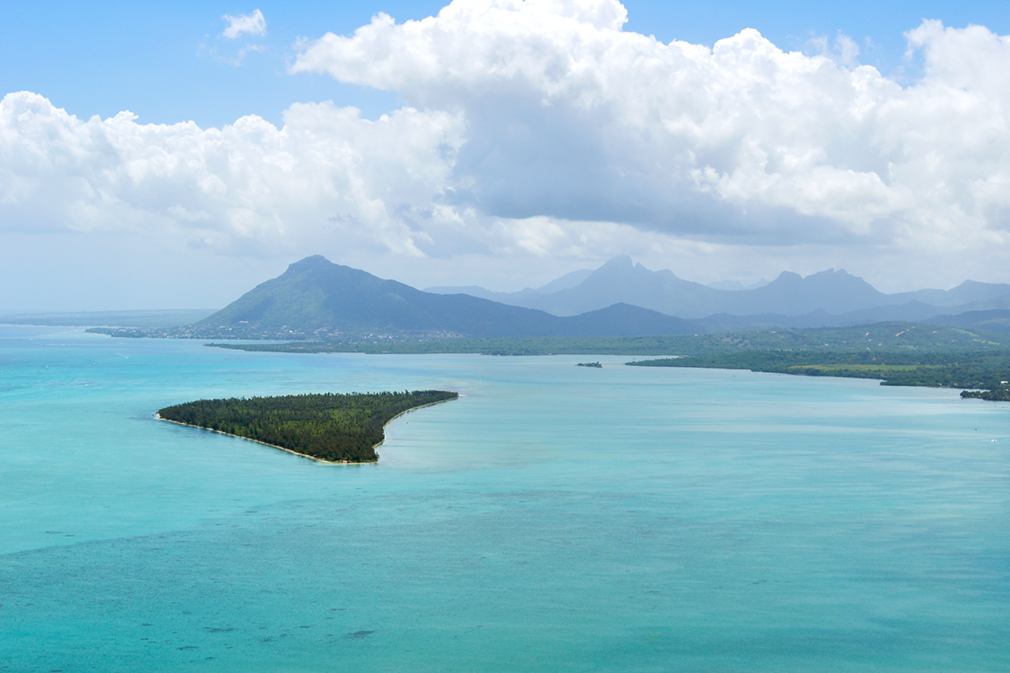 Panoramic view of turquoise waters, a forested island, and mountains